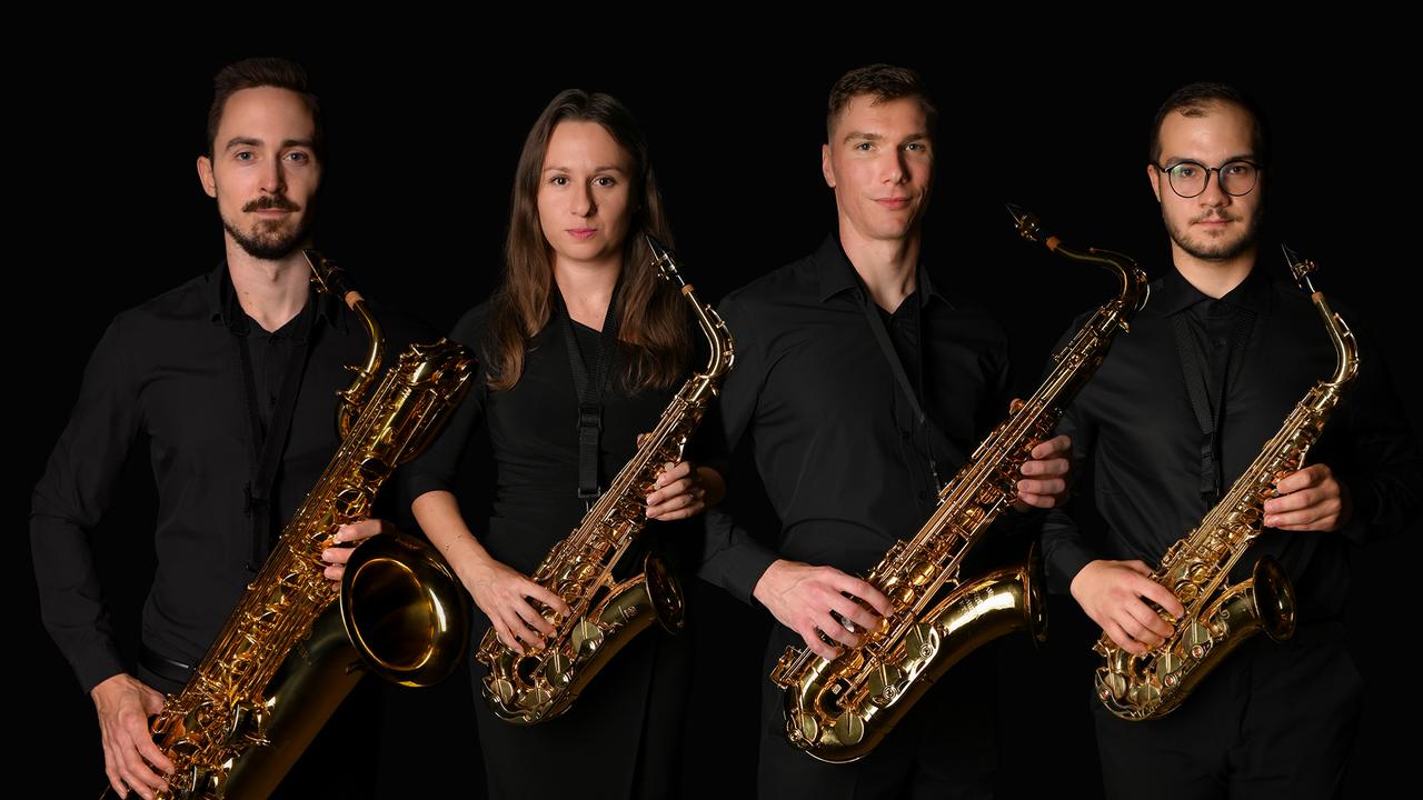 Štyria hudobníci saxofónového kvarteta v čiernom oblečení so zlatými saxofónmi na čiernom pozadí